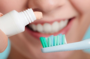 Dental health care. Closeup woman holding toothbrush and placing toothpaste on it smiling face in the background